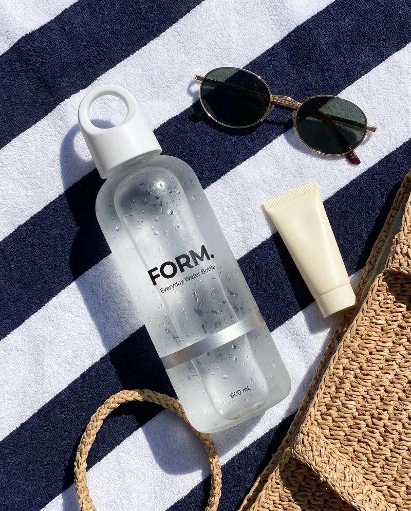 The FORM. water bottle on a striped beach towel with sunglasses and sunscreen